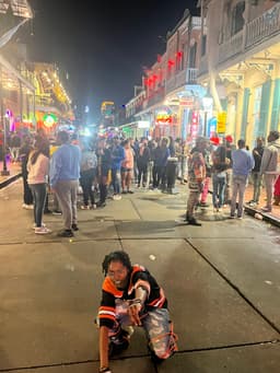 kidd squats and points at the camera as Bourbon Street sprawls behind her