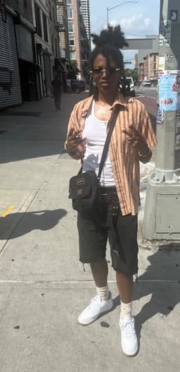 kidd throws peace to the camera as she stands on a corner in Harlem