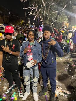 kidd stands with two younger cousins on either side of her. they are outdoors in New Orleans at a Mardi Gras parade. a sea of people is captured behind them